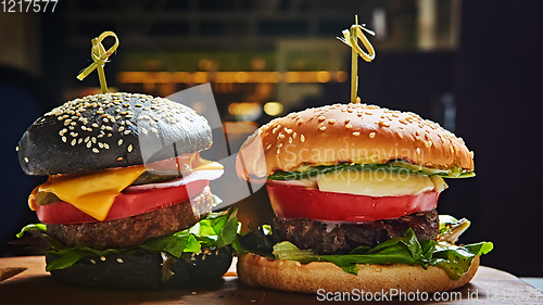 Image of Set of homemade burgers in black and white buns with tomato, lettuce, cheese, onion on wood serving board over dark table. Rustic style. Homemade fast food.