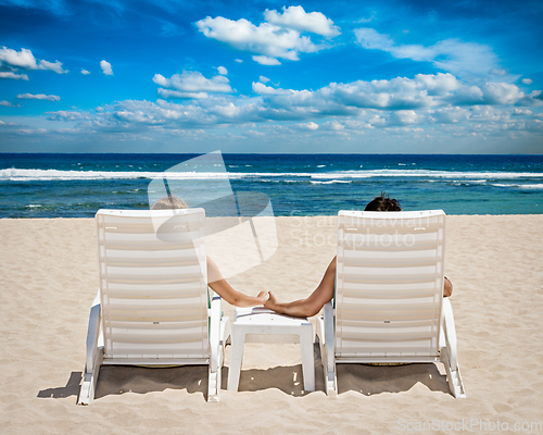 Image of Couple in beach chairs holding hands near ocean