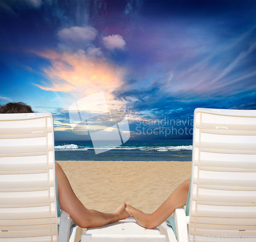 Image of Couple in beach chairs holding hands near ocean