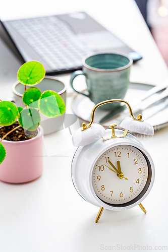 Image of Time management and procrastination concept. Composition with alarm clock on white desk, laptop computer