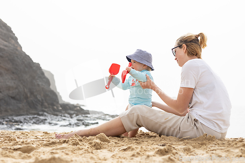 Image of Mother playing his infant baby boy son on sandy beach enjoying summer vacationson on Lanzarote island, Spain. Family travel and vacations concept.