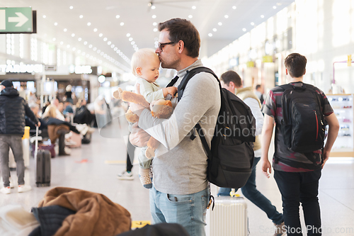 Image of Father traveling with child, holding and kising his infant baby boy at airport terminal waiting to board a plane. Travel with kids concept.