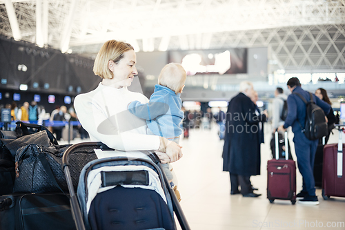 Image of Motherat travelling with his infant baby boy child, walking, pushing baby stroller and luggage cart at airport terminal station. Travel with child concept.