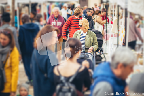 Image of Mother waling and pushing his infant baby boy child in stroller in crowd of unrecognizable people wisiting sunday flea market in Malaga, Spain.