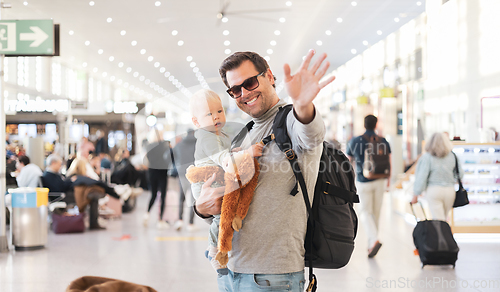 Image of Father traveling with child, holding his infant baby boy at airport terminal waiting to board a plane waving goodby. Travel with kids concept.