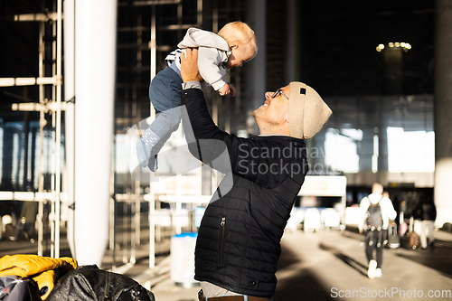 Image of Father happily holding and lifting his infant baby boy child in the air after being rejunited in front of airport terminal station. Baby travel concept.