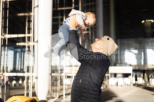 Image of Father happily holding and lifting his infant baby boy child in the air after being rejunited in front of airport terminal station. Baby travel concept.