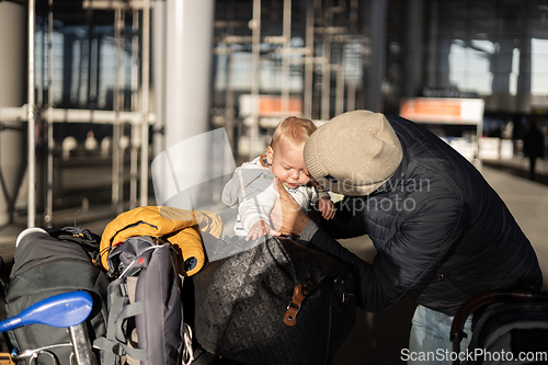 Image of Fatherat comforting his crying infant baby boy child tired sitting on top of luggage cart in front of airport terminal station while traveling wih family.