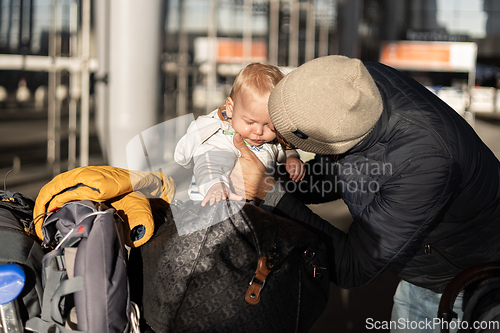 Image of Fatherat comforting his crying infant baby boy child tired sitting on top of luggage cart in front of airport terminal station while traveling wih family.