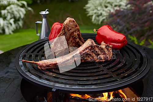 Image of Tomahawk rib beef steak and T-bone on hot black grill.