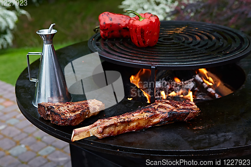 Image of Tomahawk rib beef steak and T-bone on hot black grill.