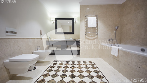 Image of Nice bathroom in a modern style with gray tiled walls. There is a white bath with a glass partition, shower, mirrors, light sink, toilet and a bidet, luminous lamps