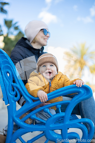 Image of Young mother with her cute infant baby boy child on bench in city park.