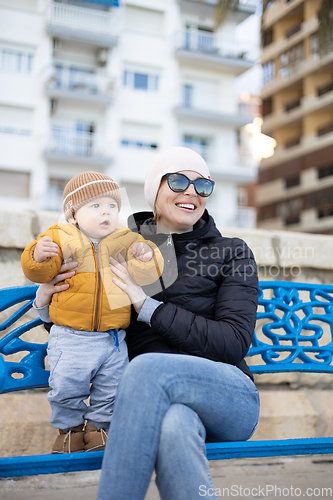 Image of Young mother with her cute infant baby boy child on bench in city park.