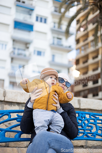 Image of Young mother with her cute infant baby boy child on bench in city park.