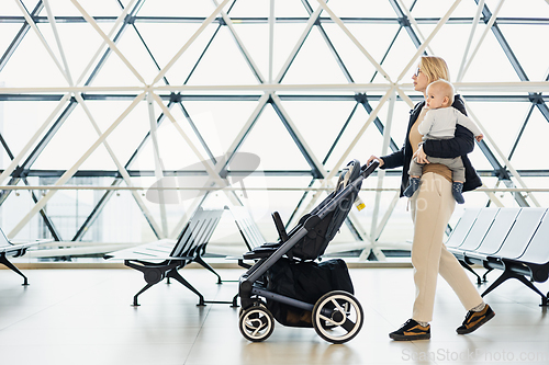 Image of Mother carying his infant baby boy child, pushing stroller at airport departure terminal moving to boarding gates to board an airplane. Family travel with baby concept.