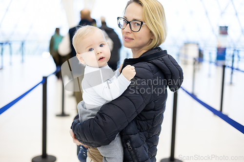 Image of Mother carying his infant baby boy child queuing at airport terminal in passport control line at immigrations departure before moving to boarding gates to board an airplane. Travel with baby concept.