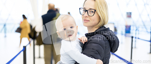 Image of Mother carying his infant baby boy child queuing at airport terminal in passport control line at immigrations departure before moving to boarding gates to board an airplane. Travel with baby concept.