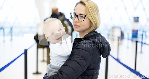 Image of Mother carying his infant baby boy child queuing at airport terminal in passport control line at immigrations departure before moving to boarding gates to board an airplane. Travel with baby concept.