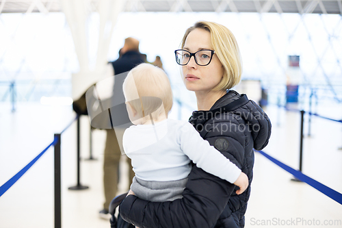 Image of Mother carying his infant baby boy child queuing at airport terminal in passport control line at immigrations departure before moving to boarding gates to board an airplane. Travel with baby concept.