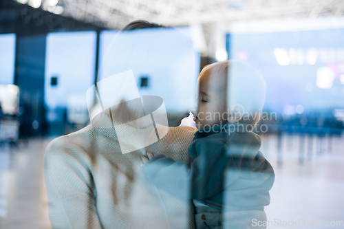 Image of Thoughtful young mother kissing and caressing his infant baby boy child while waiting by the window at airport terminal departure gates. Travel with baby concept.