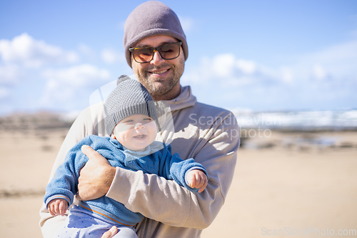 Image of Father enjoying pure nature holding and playing with his infant baby boy son in on windy sandy beach of Famara, Lanzarote island, Spain. Family travel and parenting concept.