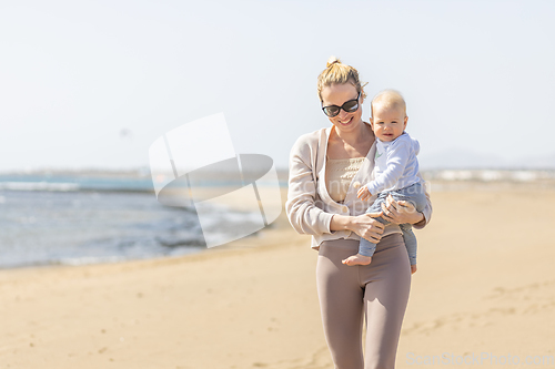 Image of Mother holding and carrying his infant baby boy son on sandy beach enjoying summer vacationson on Lanzarote island, Spain. Family travel and vacations concept.