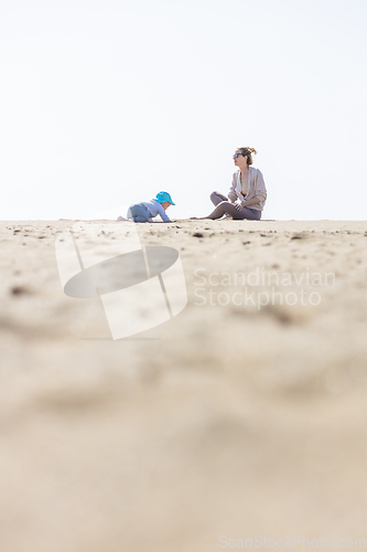 Image of Mother playing his infant baby boy son on sandy beach enjoying summer vacationson on Lanzarote island, Spain. Family travel and vacations concept.