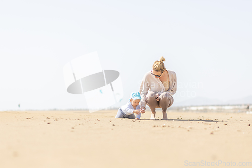 Image of Mother playing his infant baby boy son on sandy beach enjoying summer vacationson on Lanzarote island, Spain. Family travel and vacations concept.