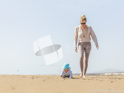 Image of Mother playing his infant baby boy son on sandy beach enjoying summer vacationson on Lanzarote island, Spain. Family travel and vacations concept.