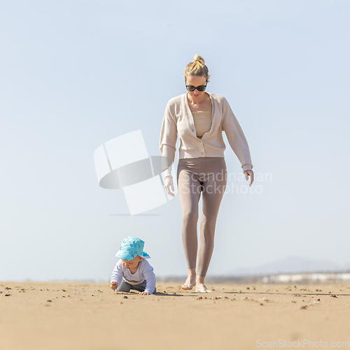 Image of Mother playing his infant baby boy son on sandy beach enjoying summer vacationson on Lanzarote island, Spain. Family travel and vacations concept.