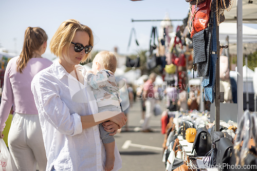 Image of Mother hoding his infant baby boy child whilechecing items at sunday flea market.