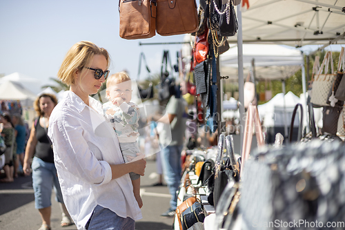 Image of Mother hoding his infant baby boy child whilechecing items at sunday flea market.