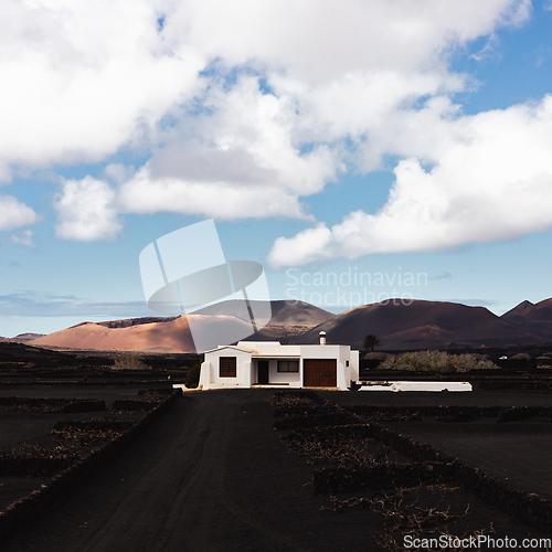 Image of Traditional white house in black volcanic landscape of La Geria wine growing region with view of Timanfaya National Park in Lanzarote. Touristic attraction in Lanzarote island, Canary Islands, Spain.