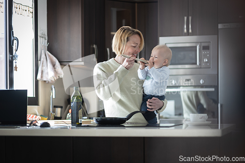 Image of Happy mother and little infant baby boy cooking and tasting healthy dinner in domestic kitchen. Family, lifestyle, domestic life, food, healthy eating and people concept.