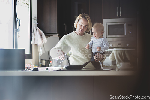 Image of Happy mother and little infant baby boy together making pancakes for breakfast in domestic kitchen. Family, lifestyle, domestic life, food, healthy eating and people concept.