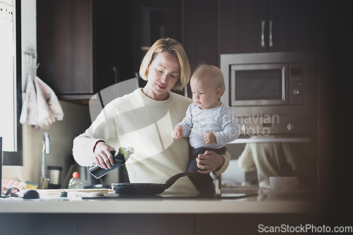 Image of Happy mother and little infant baby boy together making pancakes for breakfast in domestic kitchen. Family, lifestyle, domestic life, food, healthy eating and people concept.