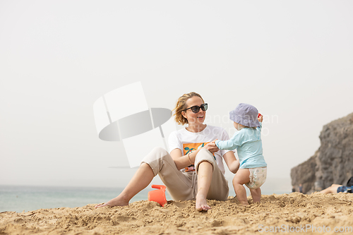 Image of Mother playing his infant baby boy son on sandy beach enjoying summer vacationson on Lanzarote island, Spain. Family travel and vacations concept.