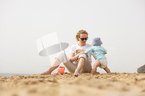 Image of Mother playing his infant baby boy son on sandy beach enjoying summer vacationson on Lanzarote island, Spain. Family travel and vacations concept.