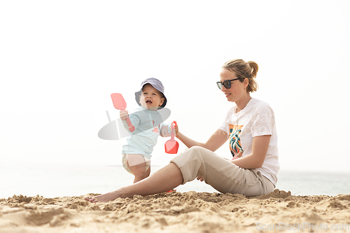 Image of Mother playing his infant baby boy son on sandy beach enjoying summer vacationson on Lanzarote island, Spain. Family travel and vacations concept.