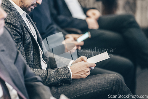 Image of Businessman hands holding meeting brochure with program and schedules of business conference lectures. Event participants in conference hall.