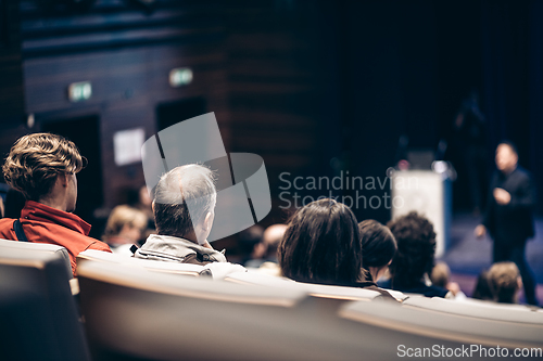 Image of Speaker giving a talk in conference hall at business event. Rear view of unrecognizable people in audience at the conference hall. Business and entrepreneurship concept.