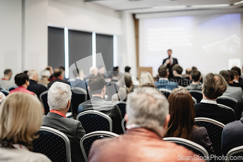 Image of Speaker giving a talk in conference hall at business event. Rear view of unrecognizable people in audience at the conference hall. Business and entrepreneurship concept.