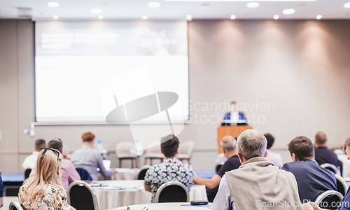 Image of Speaker giving a talk in conference hall at business event. Rear view of unrecognizable people in audience at the conference hall. Business and entrepreneurship concept.