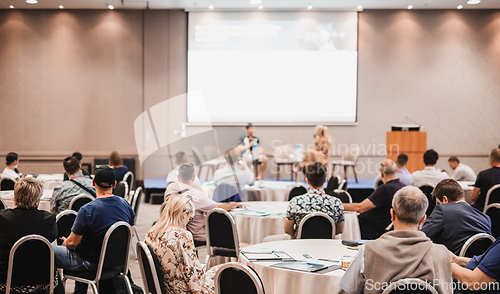 Image of Speaker giving a talk in conference hall at business event. Rear view of unrecognizable people in audience at the conference hall. Business and entrepreneurship concept.