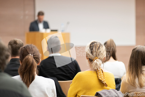 Image of Speaker giving a talk in conference hall at business event. Rear view of unrecognizable people in audience at the conference hall. Business and entrepreneurship concept.