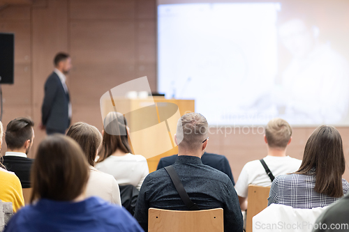 Image of Speaker giving a talk in conference hall at business event. Rear view of unrecognizable people in audience at the conference hall. Business and entrepreneurship concept.