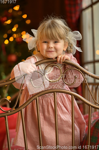 Image of Little cute blond girl standing at headboard of iron bed