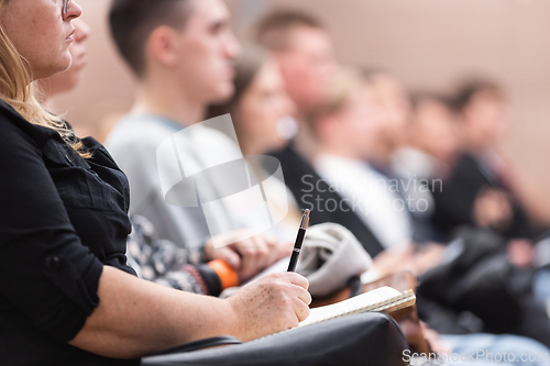 Image of Female hands holding pen and notebook, making notes at conference lecture. Event participants in conference hall.