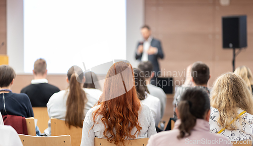 Image of Speaker giving a talk in conference hall at business event. Rear view of unrecognizable people in audience at the conference hall. Business and entrepreneurship concept.